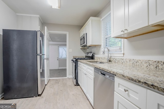 kitchen with a sink, stainless steel appliances, light wood-style floors, light stone counters, and white cabinets