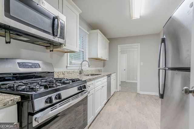 kitchen with white cabinets, stainless steel appliances, light wood-style flooring, and a sink