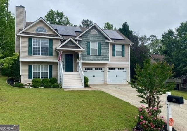 bi-level home featuring a chimney, roof mounted solar panels, driveway, a front lawn, and an attached garage