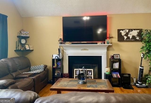 living area featuring wood finished floors, a textured ceiling, lofted ceiling, and a fireplace