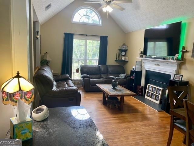 living room with a fireplace with flush hearth, lofted ceiling, a ceiling fan, visible vents, and wood finished floors