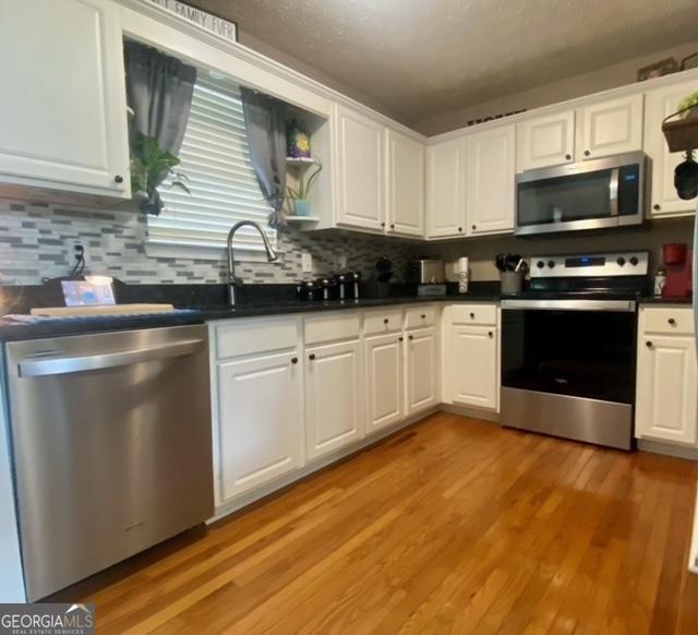 kitchen featuring dark countertops, white cabinetry, stainless steel appliances, and decorative backsplash