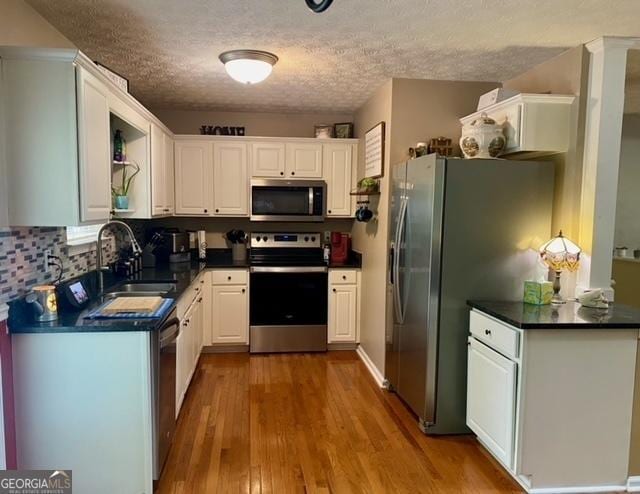 kitchen featuring stainless steel appliances, dark countertops, a textured ceiling, and wood finished floors