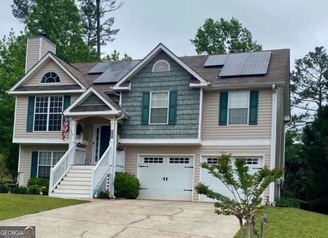 split foyer home featuring driveway, a chimney, roof mounted solar panels, and an attached garage