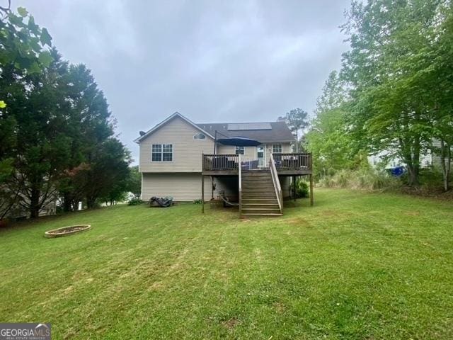 back of property featuring a deck, stairway, a fire pit, and a yard