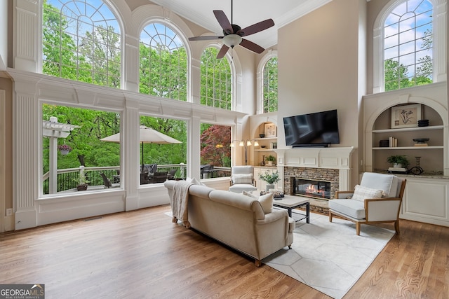 945 Hampton Bluff Dr, Milton, GA 30004 - living room featuring a high ceiling, a stone fireplace, light wood-style flooring, a ceiling fan, and ornamental molding