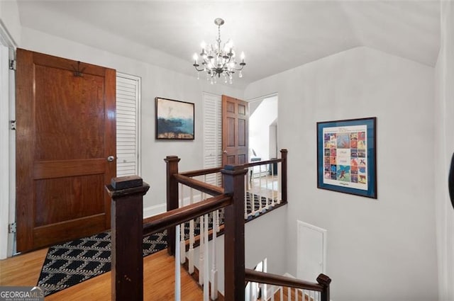 corridor featuring light wood finished floors, an upstairs landing, a notable chandelier, and lofted ceiling