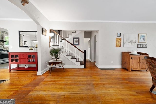 entryway with stairway, baseboards, arched walkways, ornamental molding, and light wood finished floors