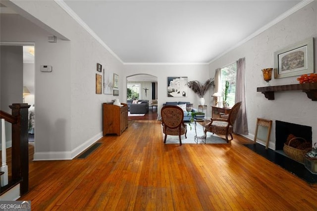 living area featuring arched walkways, wood-type flooring, visible vents, a fireplace with flush hearth, and crown molding