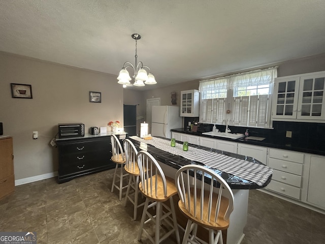 kitchen with white cabinetry, a notable chandelier, dark countertops, and freestanding refrigerator