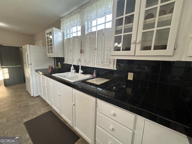 kitchen featuring tasteful backsplash, glass insert cabinets, freestanding refrigerator, a sink, and white cabinetry