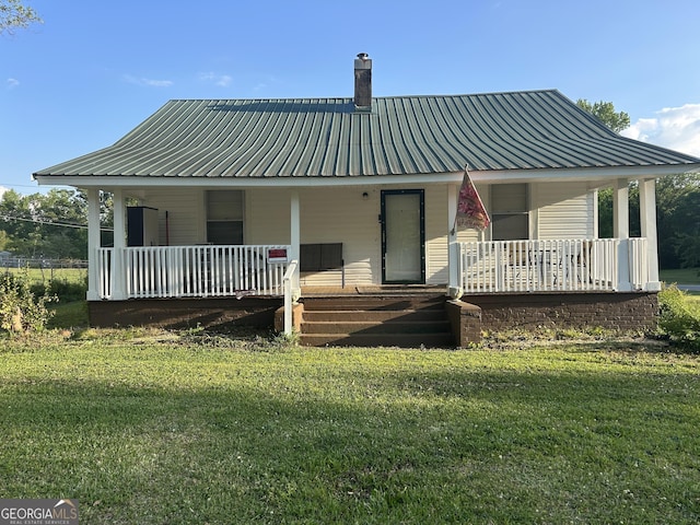 rear view of property with a lawn, a chimney, metal roof, and a porch