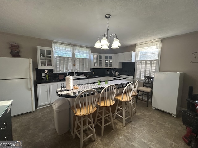 kitchen featuring glass insert cabinets, dark countertops, a kitchen island, freestanding refrigerator, and a notable chandelier