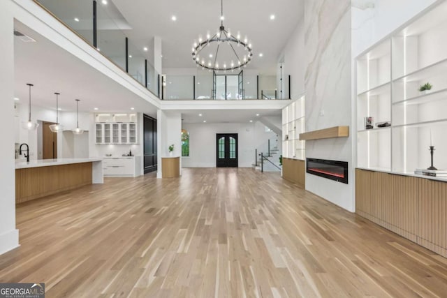 1255 E M Croy Rd, Sugar Hill, GA 30518 - unfurnished living room with a high ceiling, light wood-style flooring, a glass covered fireplace, a chandelier, and recessed lighting
