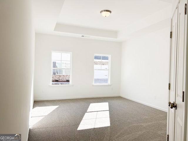 carpeted empty room featuring a raised ceiling, baseboards, and visible vents