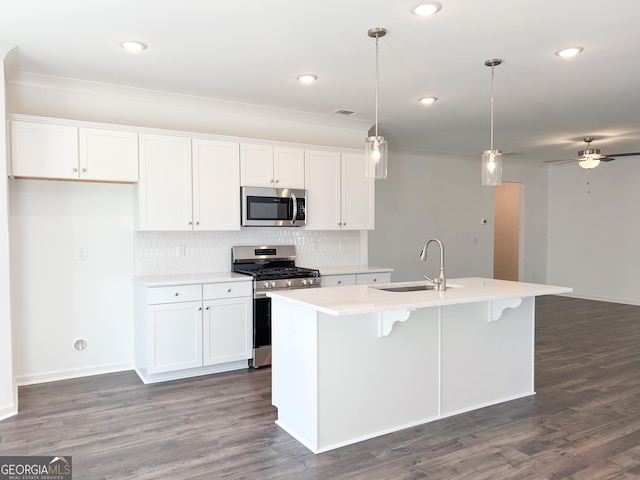 kitchen with white cabinets, appliances with stainless steel finishes, a sink, backsplash, and a center island with sink