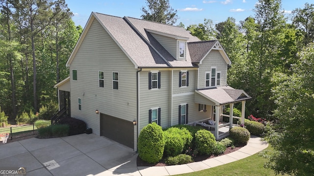 view of side of property with an attached garage, fence, driveway, and roof with shingles