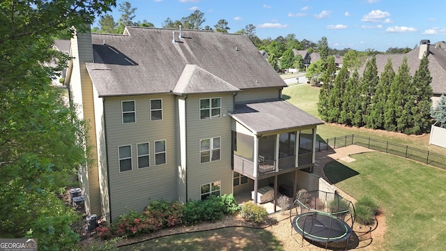 rear view of house featuring fence, roof with shingles, a sunroom, a chimney, and a lawn