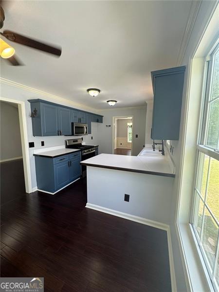955 Tributary Way, Dacula, GA 30019 - kitchen with stainless steel microwave, blue cabinetry, crown molding, a peninsula, and dark wood-style flooring