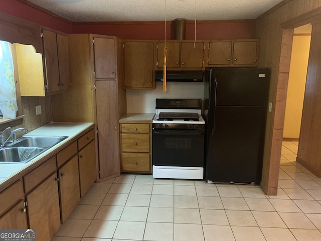 kitchen with freestanding refrigerator, light tile patterned floors, gas range, under cabinet range hood, and a sink