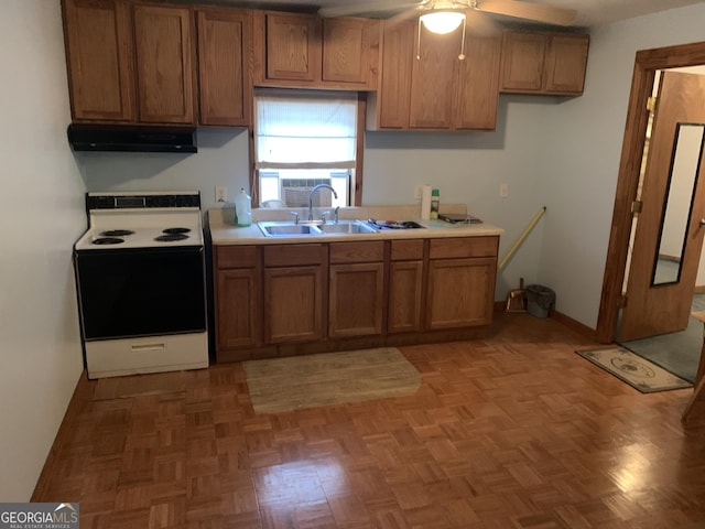 kitchen featuring brown cabinetry, electric range, under cabinet range hood, a sink, and a ceiling fan