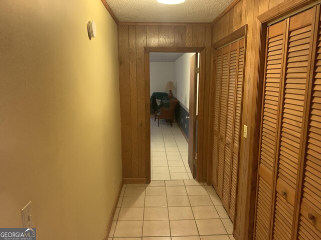 hall with light tile patterned floors, wooden walls, a textured ceiling, and ornamental molding