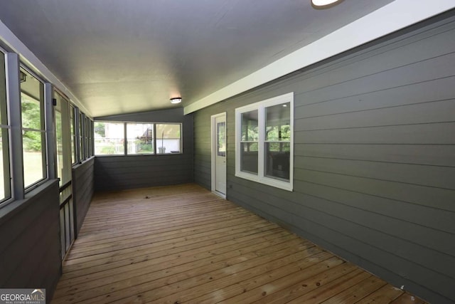 unfurnished sunroom featuring wood-type flooring, wooden walls, and lofted ceiling