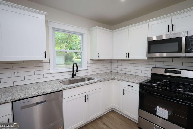 kitchen featuring a sink, light stone counters, stainless steel appliances, and white cabinetry