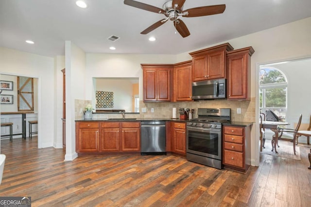 kitchen with dark countertops, ceiling fan, stainless steel appliances, decorative backsplash, and dark wood-style floors