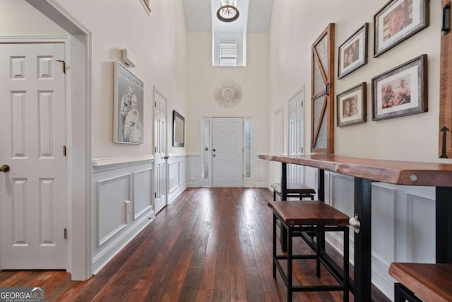 entrance foyer featuring dark wood-style flooring, a towering ceiling, and a wainscoted wall