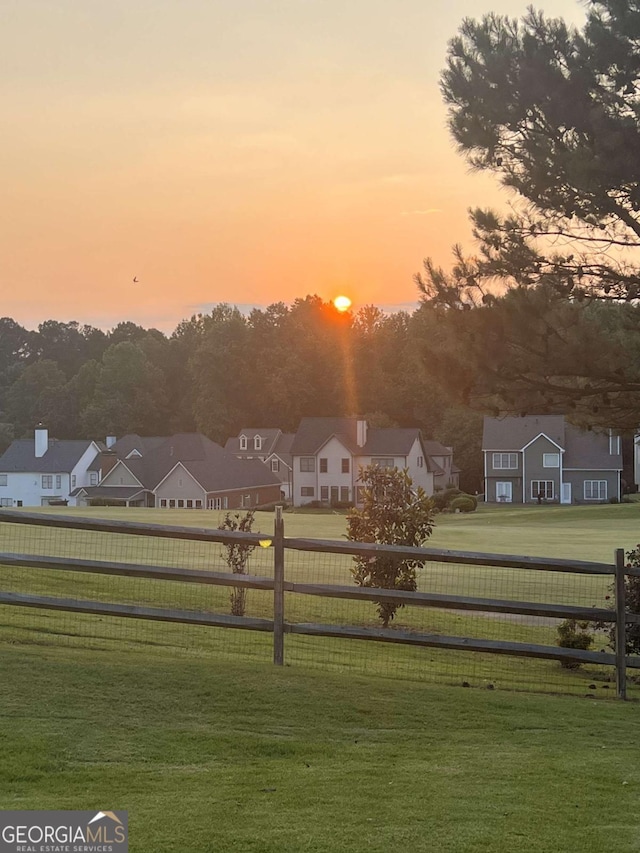 yard at dusk featuring fence and a residential view