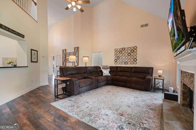 living room featuring visible vents, wood finished floors, a stone fireplace, ceiling fan, and a high ceiling