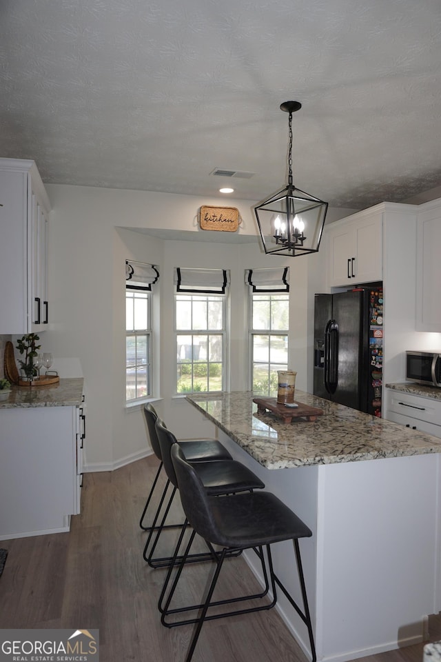2566 Summit Cove Dr, Duluth, GA 30097 - kitchen featuring black refrigerator with ice dispenser, stainless steel microwave, wood finished floors, white cabinetry, and light stone countertops