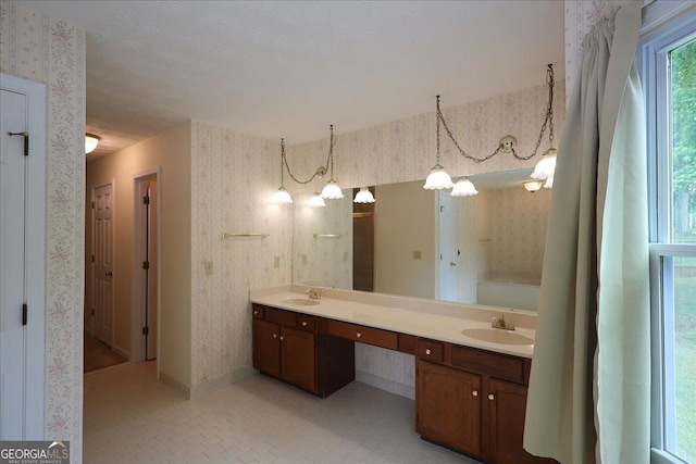full bathroom featuring a sink, baseboards, wallpapered walls, and double vanity