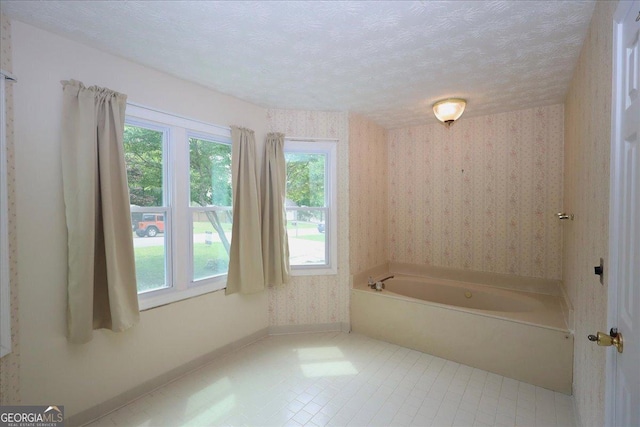 full bathroom featuring a textured ceiling, a bath, baseboards, tile patterned floors, and wallpapered walls