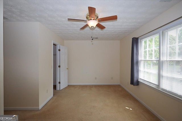 empty room featuring light colored carpet, a textured ceiling, baseboards, and ceiling fan