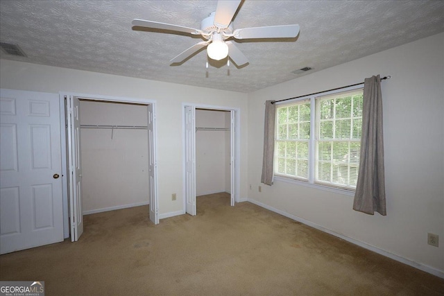 unfurnished bedroom featuring visible vents, multiple closets, baseboards, a textured ceiling, and carpet flooring