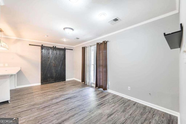 empty room with visible vents, crown molding, wood finished floors, baseboards, and a barn door