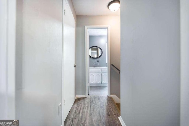 corridor with baseboards, wood finished floors, and an upstairs landing
