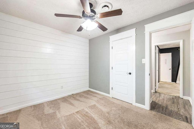 unfurnished bedroom featuring a ceiling fan, a textured ceiling, wood walls, carpet floors, and baseboards