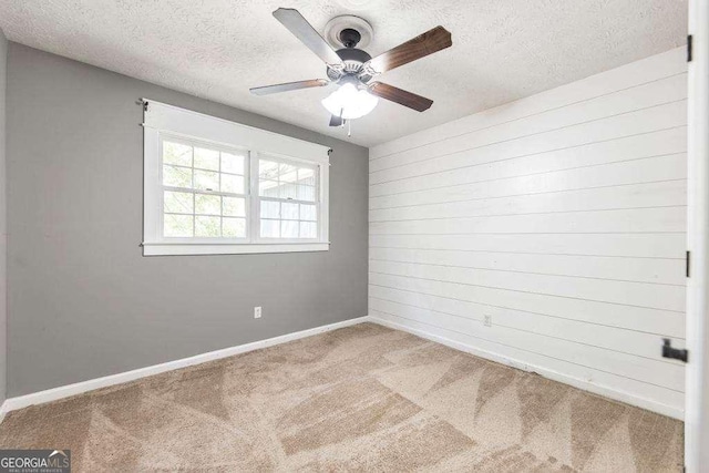 spare room featuring carpet flooring, ceiling fan, a textured ceiling, wood walls, and baseboards