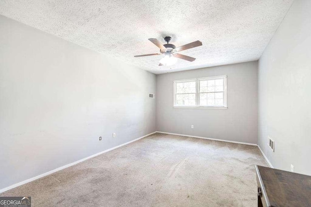 carpeted empty room featuring baseboards, a textured ceiling, ceiling fan, and visible vents