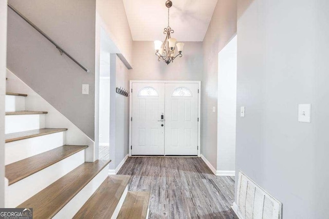 foyer featuring a notable chandelier, stairs, wood finished floors, vaulted ceiling, and visible vents