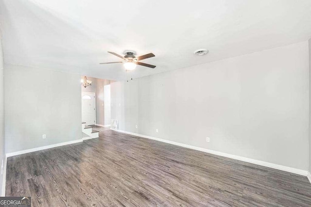 empty room featuring baseboards, ceiling fan with notable chandelier, wood finished floors, and visible vents
