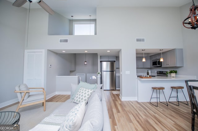 living room with a towering ceiling, visible vents, light wood-style floors, and baseboards