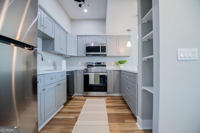 kitchen with a sink, light wood-style flooring, light countertops, gray cabinetry, and appliances with stainless steel finishes