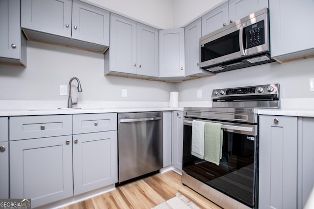 kitchen with gray cabinetry, appliances with stainless steel finishes, light wood finished floors, and a sink