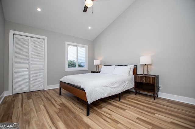 bedroom with baseboards, light wood-type flooring, a closet, and vaulted ceiling