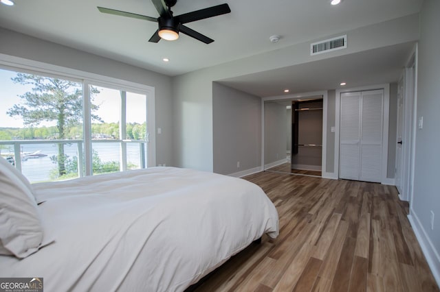 bedroom featuring recessed lighting, wood finished floors, visible vents, baseboards, and multiple closets