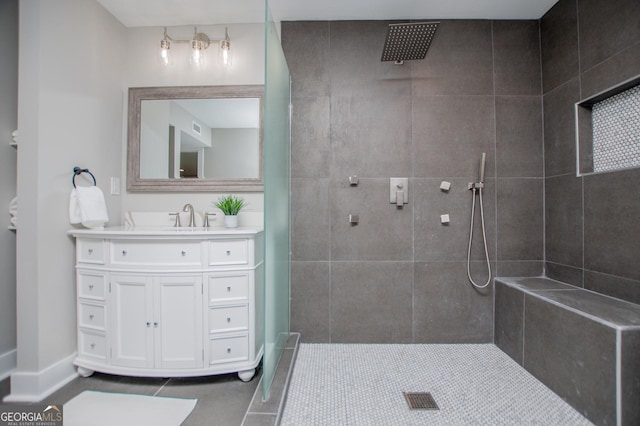 bathroom with a tile shower, tile patterned flooring, vanity, baseboards, and visible vents